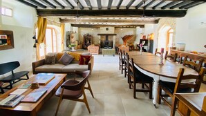 Un vaste espace de vie doté d’un plafond haut, de poutres apparentes, d’une cheminée et d’un coin repas avec des meubles en bois.