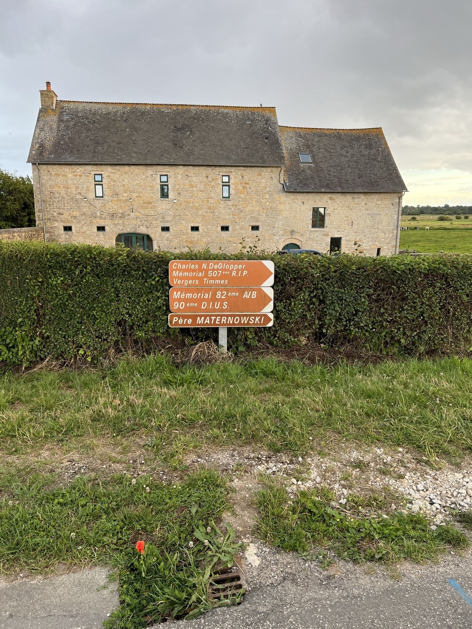 Un bâtiment en pierre sur lequel est apposée une plaque indiquant les directions vers différents monuments commémoratifs et le lieu de sépulture du père Maternowski.