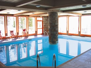 An indoor swimming pool with clear blue water, surrounded by wooden deck and stone pillars.
