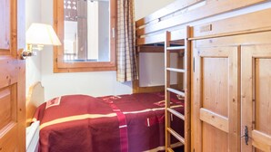 Une chambre avec un lit superposé, une armoire en bois, une fenêtre avec des rideaux et une lampe.
