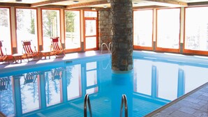 Une piscine intérieure à l’eau d’un bleu cristallin, entourée d’une terrasse en bois et de piliers en pierre.