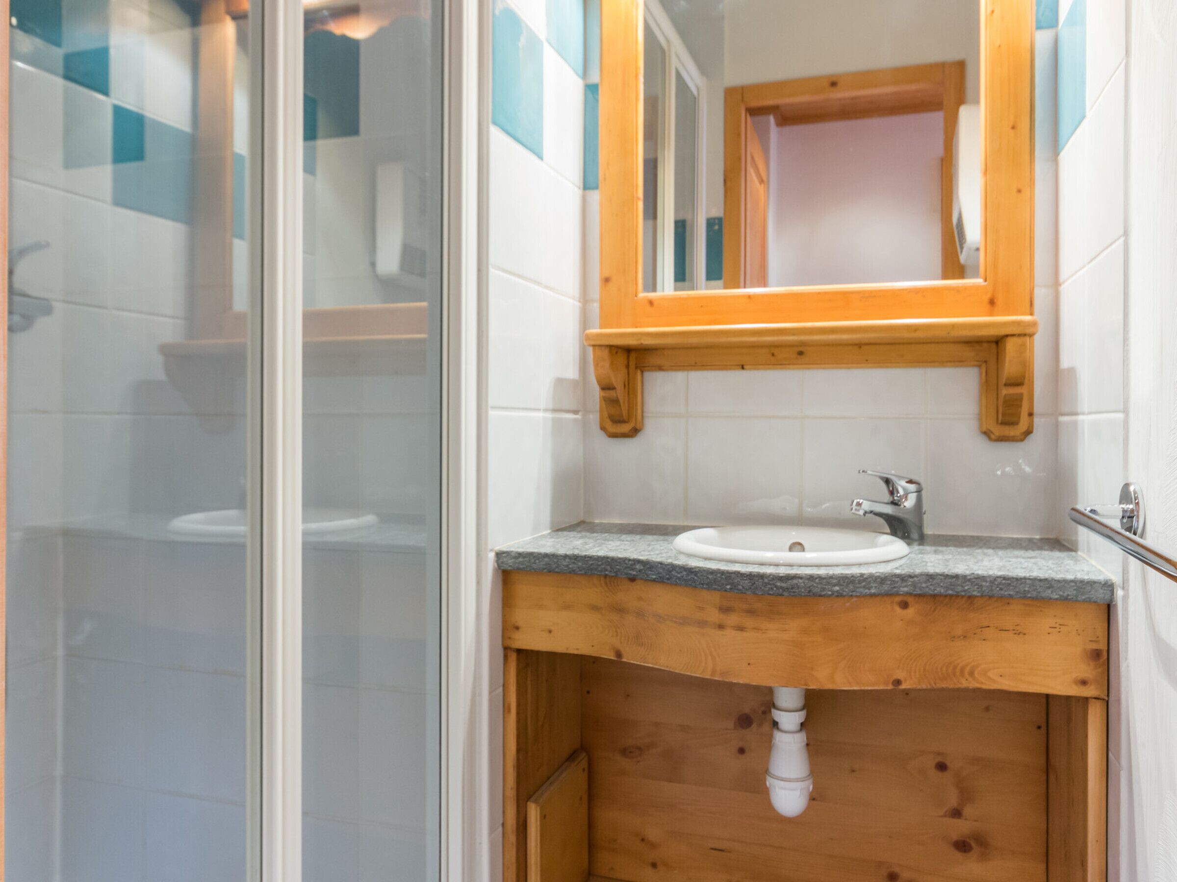 Un bagno con box doccia in vetro, un mobile bagno in legno con lavandino e uno specchio sopra il mobile.