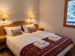 Un lit avec du linge de lit blanc, deux oreillers à motifs de rennes, un plaid rouge et blanc à motifs, et deux lampes de chevet.