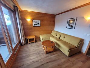 Un salon chaleureux avec un canapé, une petite table et une table basse ronde. Deux lampes murales et deux tableaux encadrés ornent les murs.