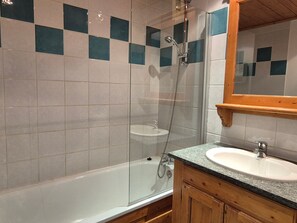 Une salle de bain dotée d’une douche à parois de verre, d’une baignoire blanche, d’un lavabo avec un plan de travail en granit et d’un meuble-lavabo en bois.