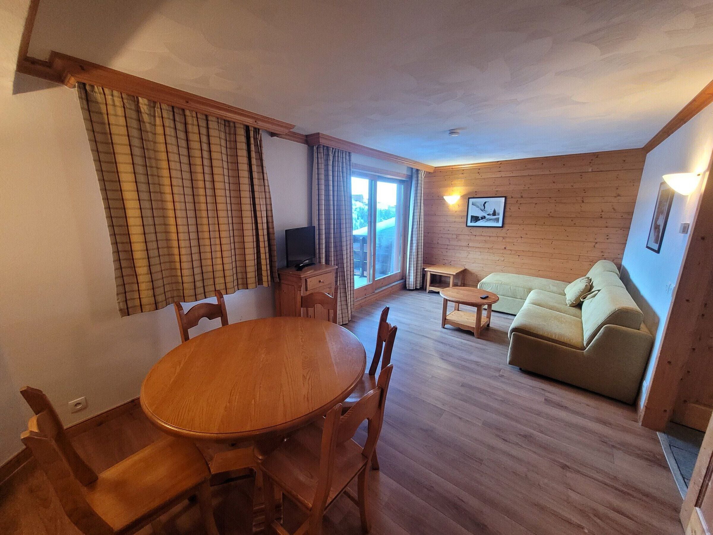 A cozy room with a wooden dining table, chairs, a sofa, and a TV.