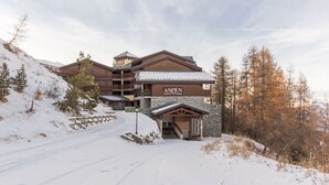 Un chalet à plusieurs étages, avec une entrée donnant sur une station de ski, des murs en pierre et une enseigne indiquant « ASPN ».