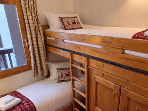 Un lit superposé avec une tête de lit en bois, une fenêtre avec des rideaux et une petite table de chevet sur laquelle est posée une serviette.
