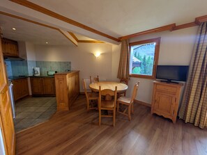 A dining area with a wooden table and chairs, a television, and a window with a view of trees.
