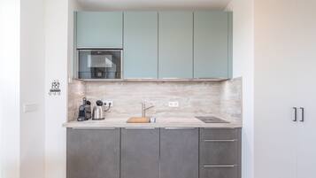 A compact kitchen with grey cabinets, a light blue upper cabinet, a stainless steel range hood, and a marble backsplash.