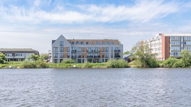 A modern building with multiple floors, large windows, and a flat roof, situated by a body of water.