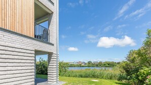 A modern building with a balcony, a grassy area, and a lake in the background.