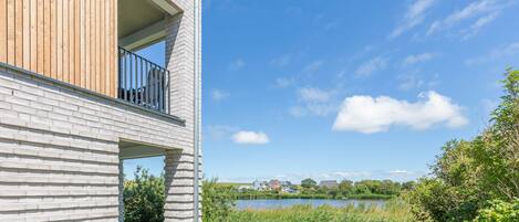 A modern building with a balcony, a grassy area, and a lake in the background.