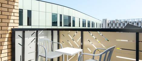 A modern outdoor seating area with two white tables and chairs, a glass partition, and a brick wall.