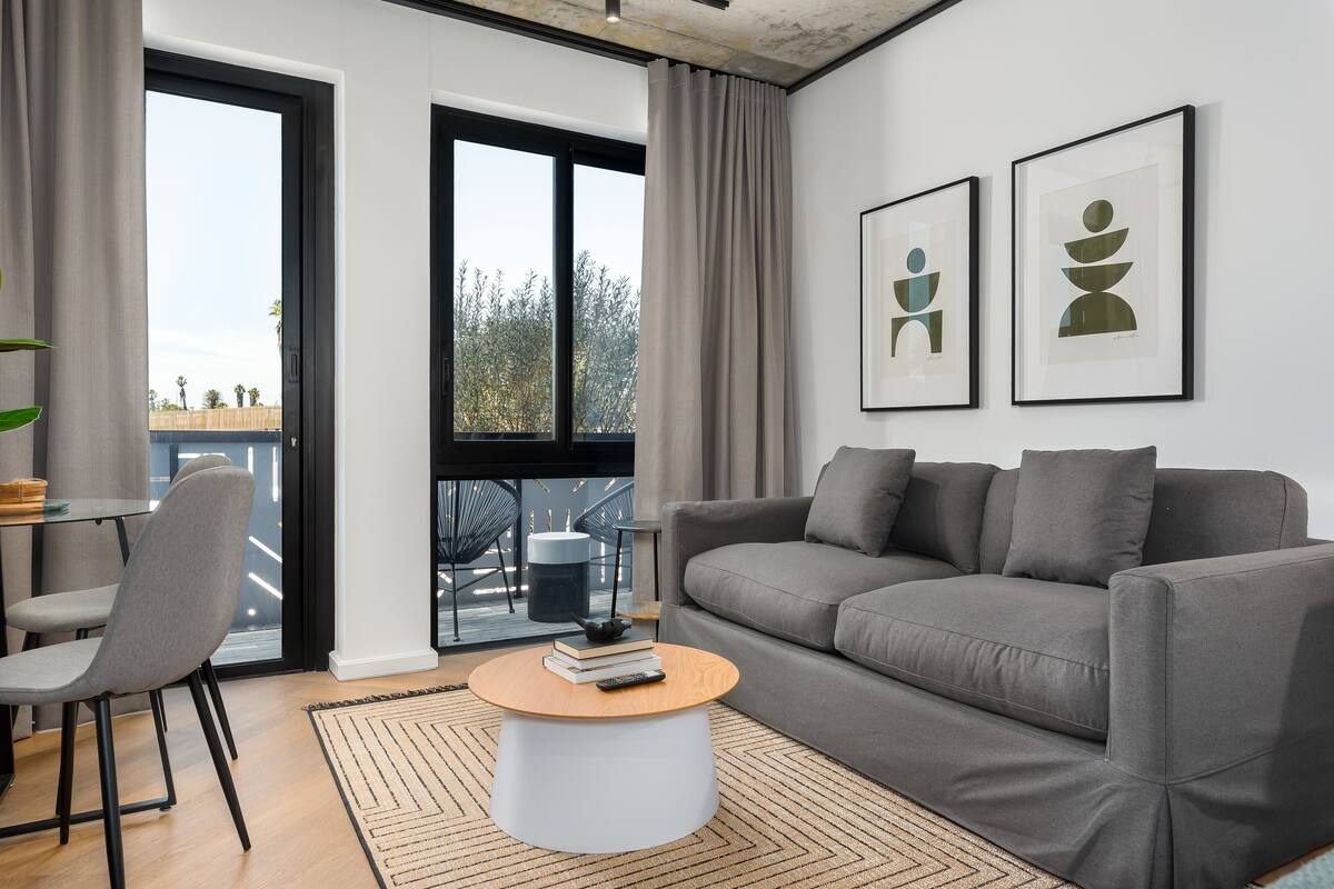 A modern living room with a grey sofa, a round coffee table, and a view of the outdoors through large windows.