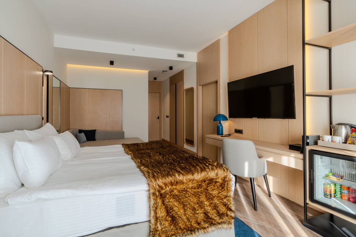 A hotel room with a large bed, a desk with a computer, a television, and a mini-fridge.