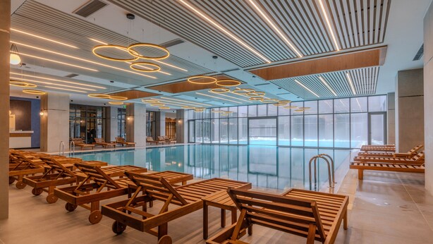 A modern indoor pool area with wooden loungers and a large glass window. - Megasaray Mount Erciyes (Kayseri)