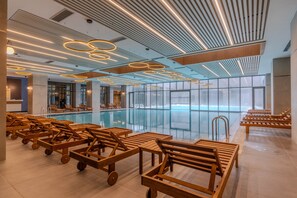 A modern indoor pool area with wooden loungers and a large glass window. - Megasaray Mount Erciyes (Kayseri)