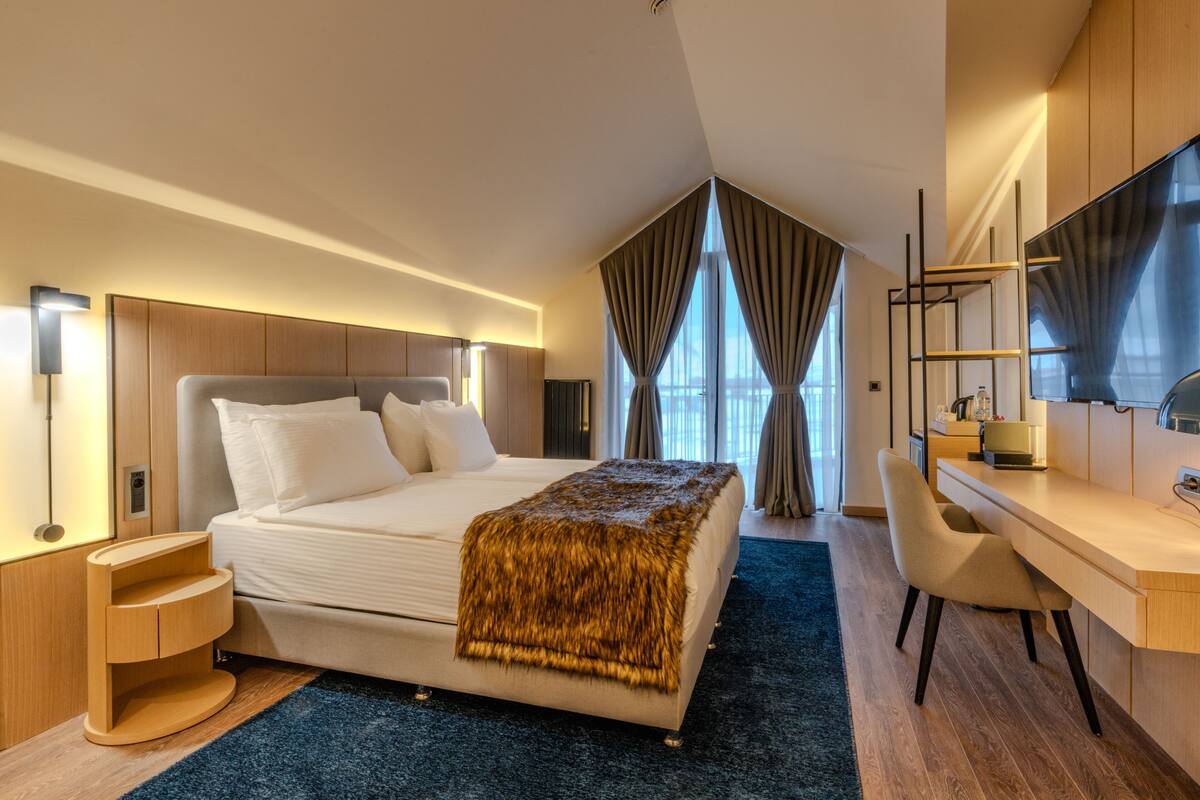 A modern hotel room with a large bed, a desk, and a chair.