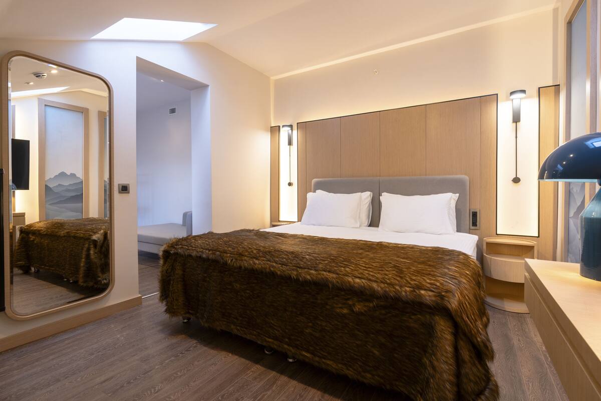 A modern hotel room with a large bed, a mirror, and a nightstand.