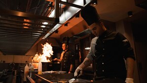 A chef preparing food in a kitchen with a visible fire, stainless steel appliances, and a high ceiling. - Megasaray Mount Erciyes (Kayseri)