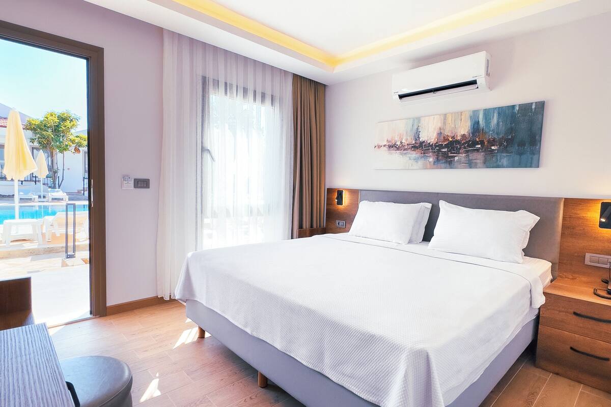 A modern hotel room with a large bed, a desk, and a view of a pool and building.