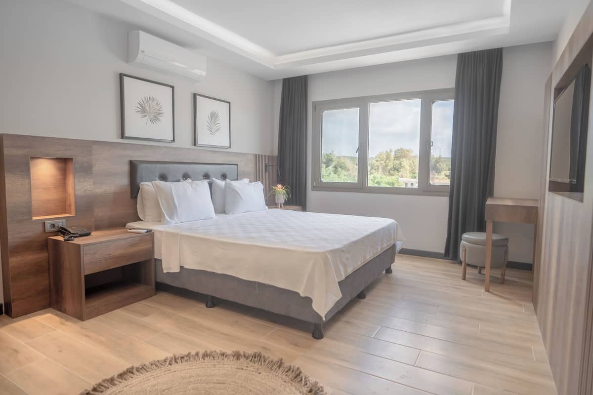 A modern bedroom with a large bed, bedside tables, a nightstand, a window with curtains, and framed artwork on the wall.