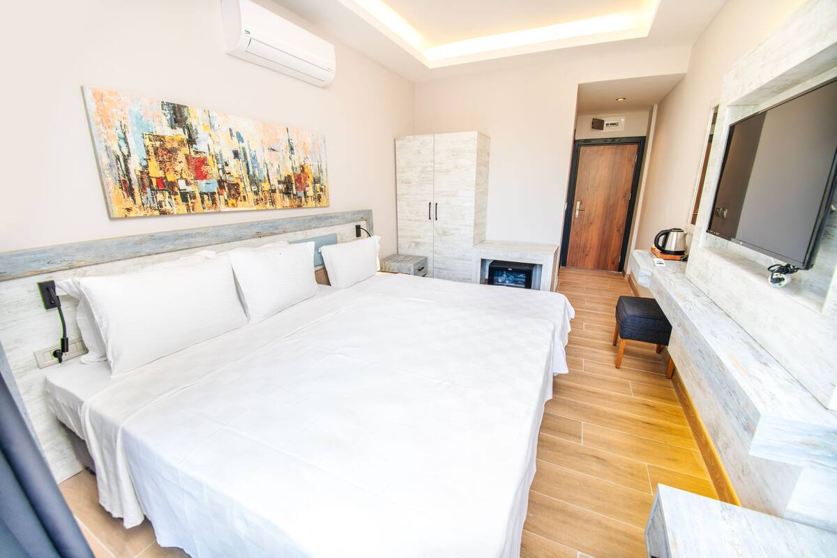 A modern hotel room with a large bed, a television, a painting on the wall, and a wooden floor.