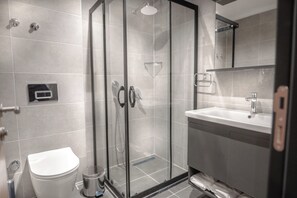 Une salle de bain moderne avec une douche à parois de verre, des toilettes blanches et un lavabo surmonté d’un miroir.