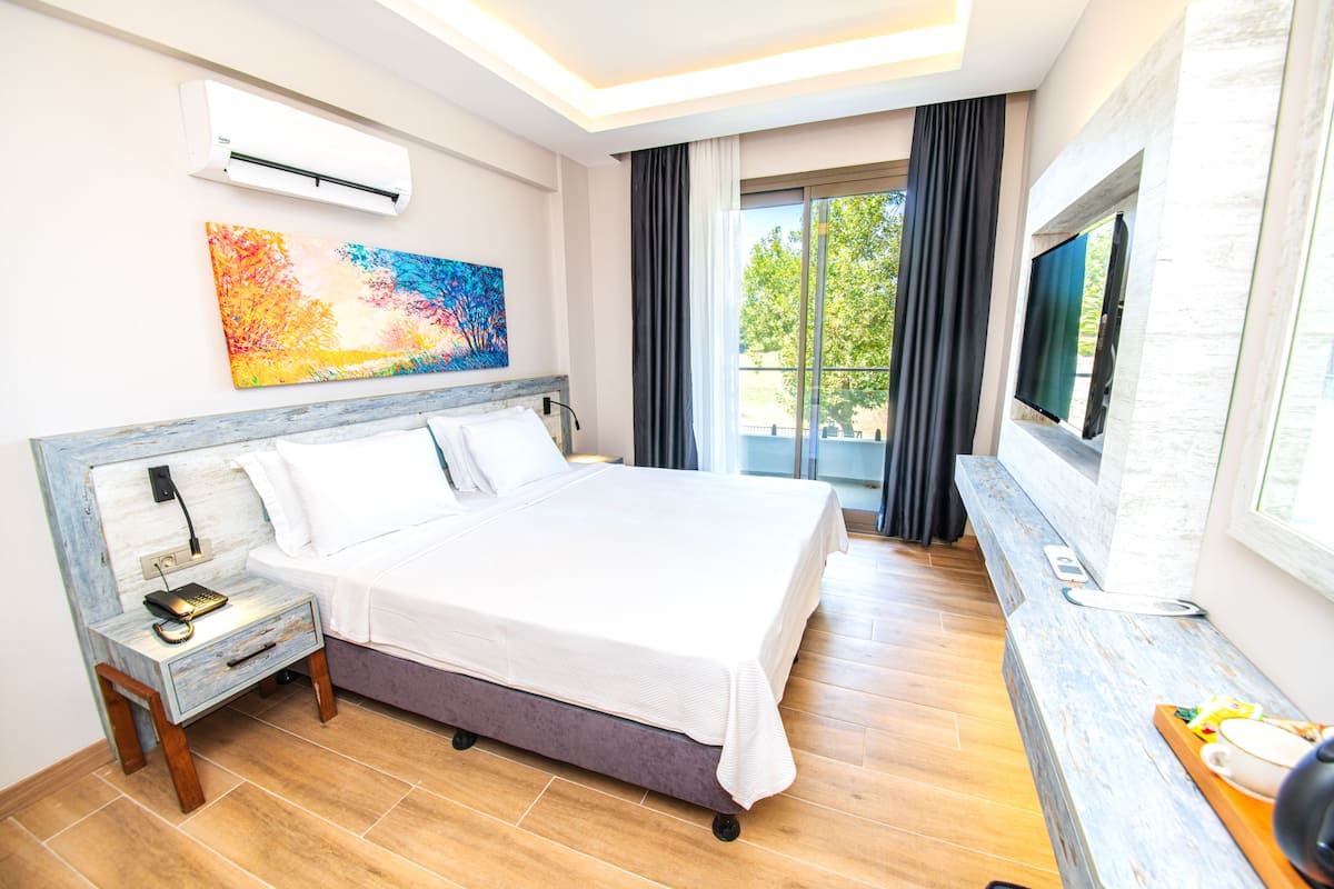 A modern hotel room with a large bed, a bedside table with a phone, a flat-screen TV, and a painting on the wall.
