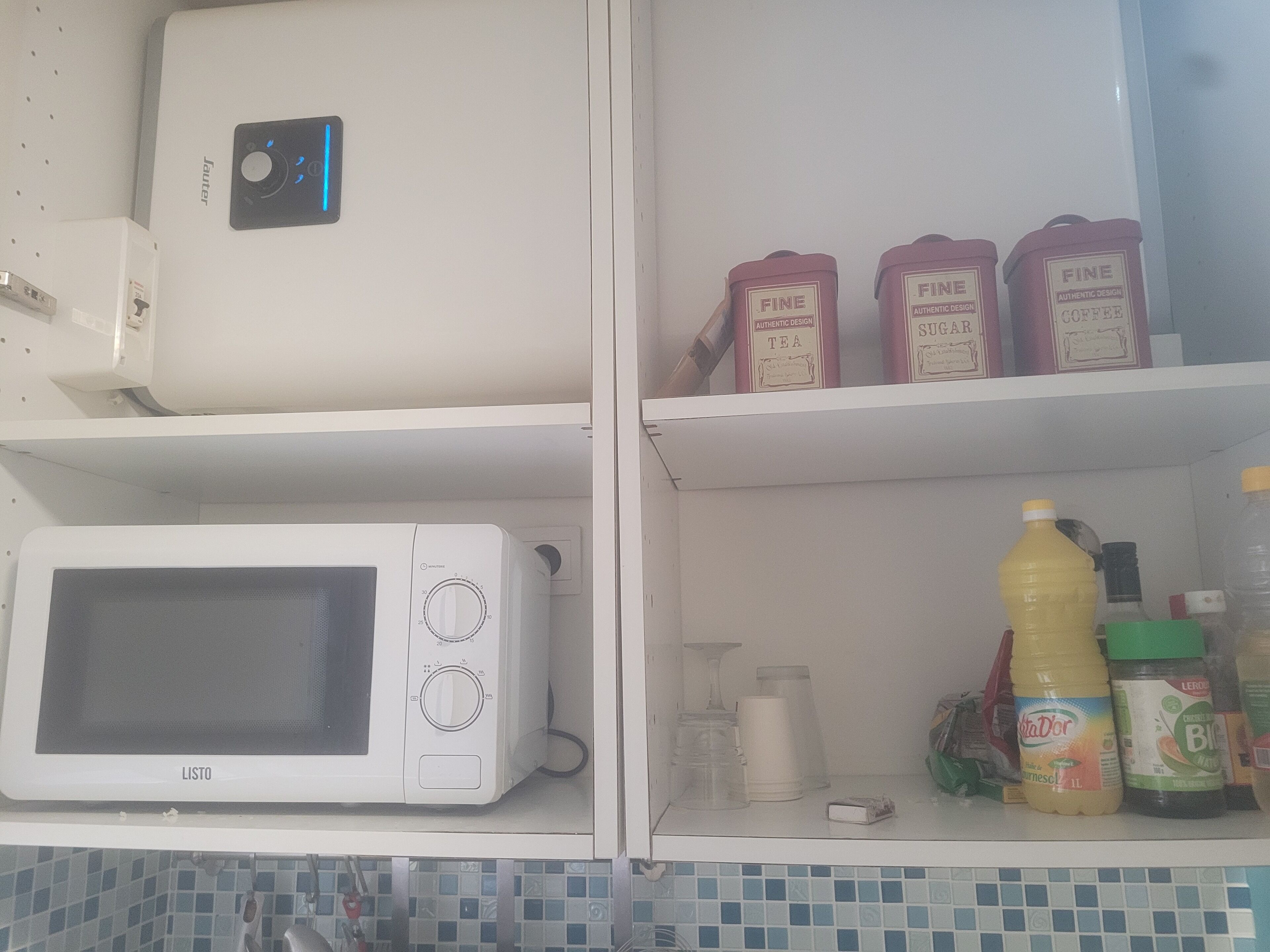 Eine Küche mit Mikrowelle, Kaffeemaschine und Regalen mit Teesorten, Zucker und Kaffee.