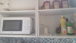 Eine Küche mit Mikrowelle, Kaffeemaschine und Regalen mit Teesorten, Zucker und Kaffee.