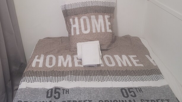 Ein Bett mit einem Kissen mit dem Schriftzug 'HOME' und einer Decke mit dem Aufdruck '05th ORIGINAL STREET'.