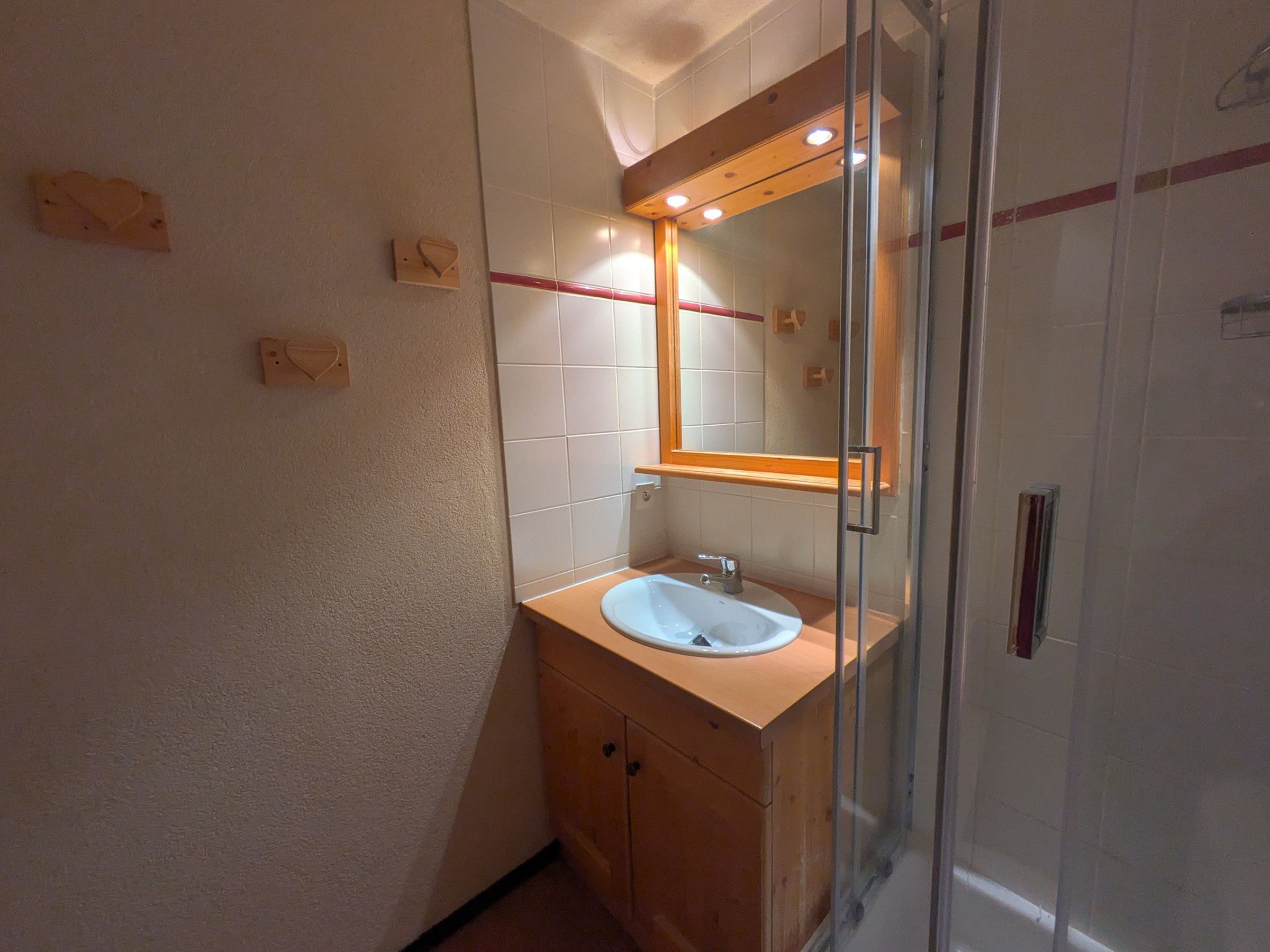 Ein Badezimmer mit einer Duschkabine aus Glas, einem Waschbecken mit Spiegel darüber und Holzschränken.