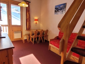 Um quarto acolhedor com uma mesa de jantar de madeira, cadeiras, um sofá vermelho e uma escada.
