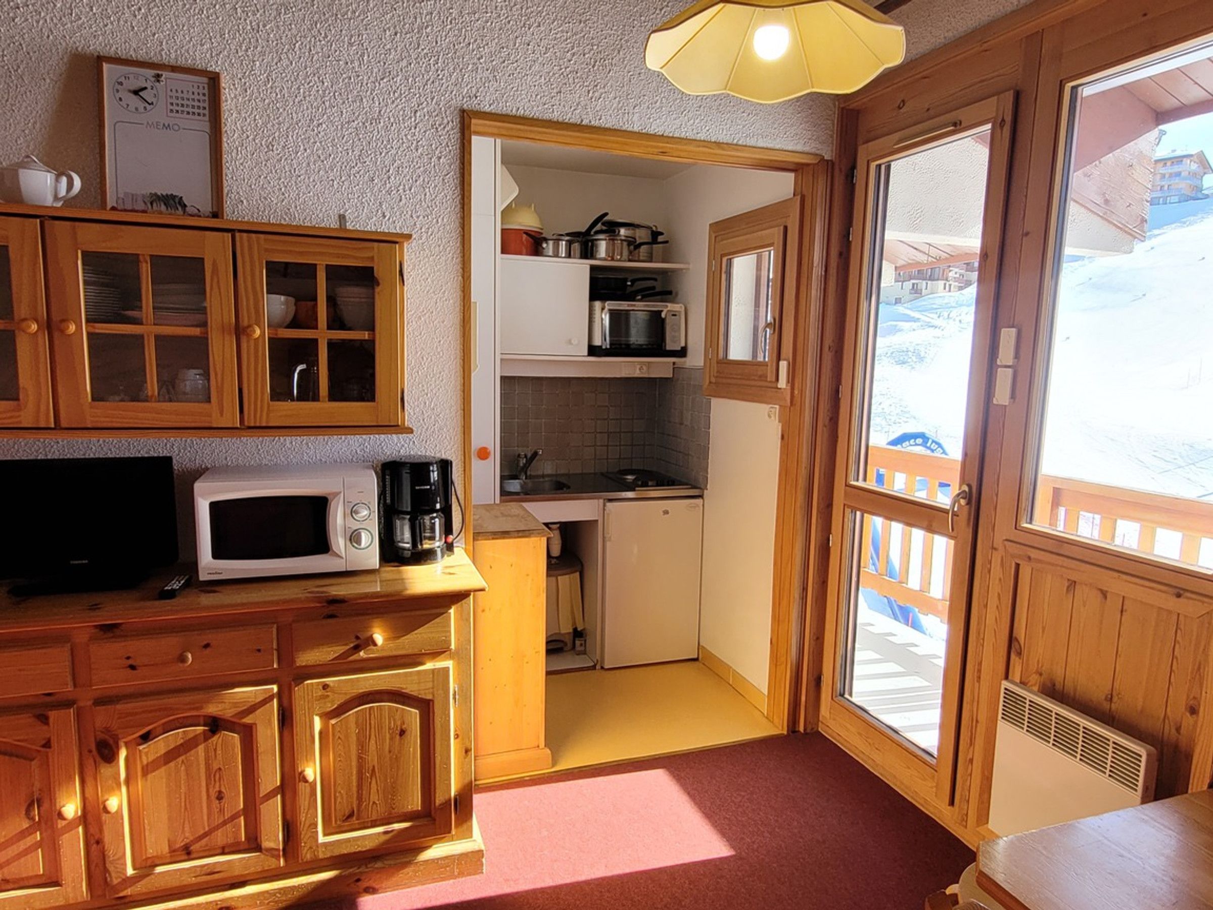 A compact kitchen with wooden cabinets, a microwave, a coffee maker, and a small refrigerator.