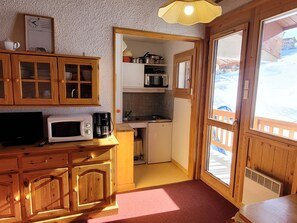A compact kitchen with wooden cabinets, a microwave, a coffee maker, and a small refrigerator.