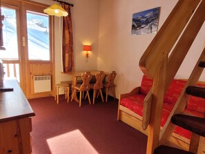 Um quarto acolhedor com uma mesa de jantar de madeira, cadeiras, um sofá vermelho e uma escada.