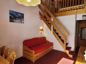 A wooden staircase leading to an upper level, a red sofa in the lower room, and a wall-mounted lamp.
