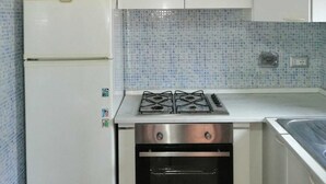 A compact kitchen with white cabinets, a white refrigerator, a gas stove, and an oven. - Cottage 30 steps from the sea (Fiumicino)