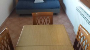 A small room with a wooden table and chairs, a blue sofa, and a cabinet with glass doors. - Cottage 30 steps from the sea (Fiumicino)