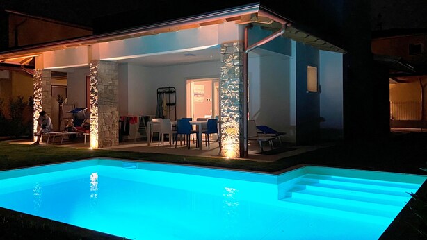 A modern outdoor pool area with a stone pillar and a covered seating area. - Villa Silvia, with private heated pool and garden. (Solarolo)