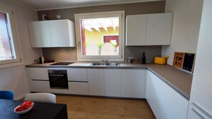 A compact kitchen with white cabinets, a built-in oven, a sink, and a window with a view of greenery. - Villa Silvia, with private heated pool and garden. (Solarolo)