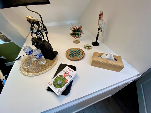 A table with a zebra figurine, a bird figurine, a small plant, a tissue box, a bottle of water, a coaster, and a card. - Le Clos de la Chapelle (Bayeux)