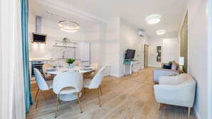 A modern living room with a sofa, a dining area with a table set for four, and a kitchen with a built-in oven and a TV. - Apartamenty Sun & Snow Double Rest (Wladyslawowo)