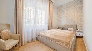 A bedroom with a bed, a chair, a nightstand, and sheer curtains. - Apartamenty Sun & Snow Double Rest (Wladyslawowo)