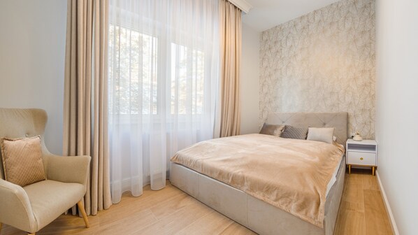 A bedroom with a bed, a chair, a nightstand, and sheer curtains.