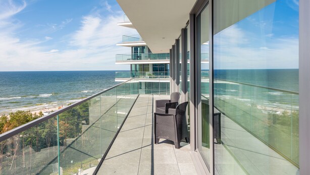 A balcony with a glass railing overlooking a beach and ocean. - Prywatne Apartamenty Sun & Snow w Wave (Miedzyzdroje)