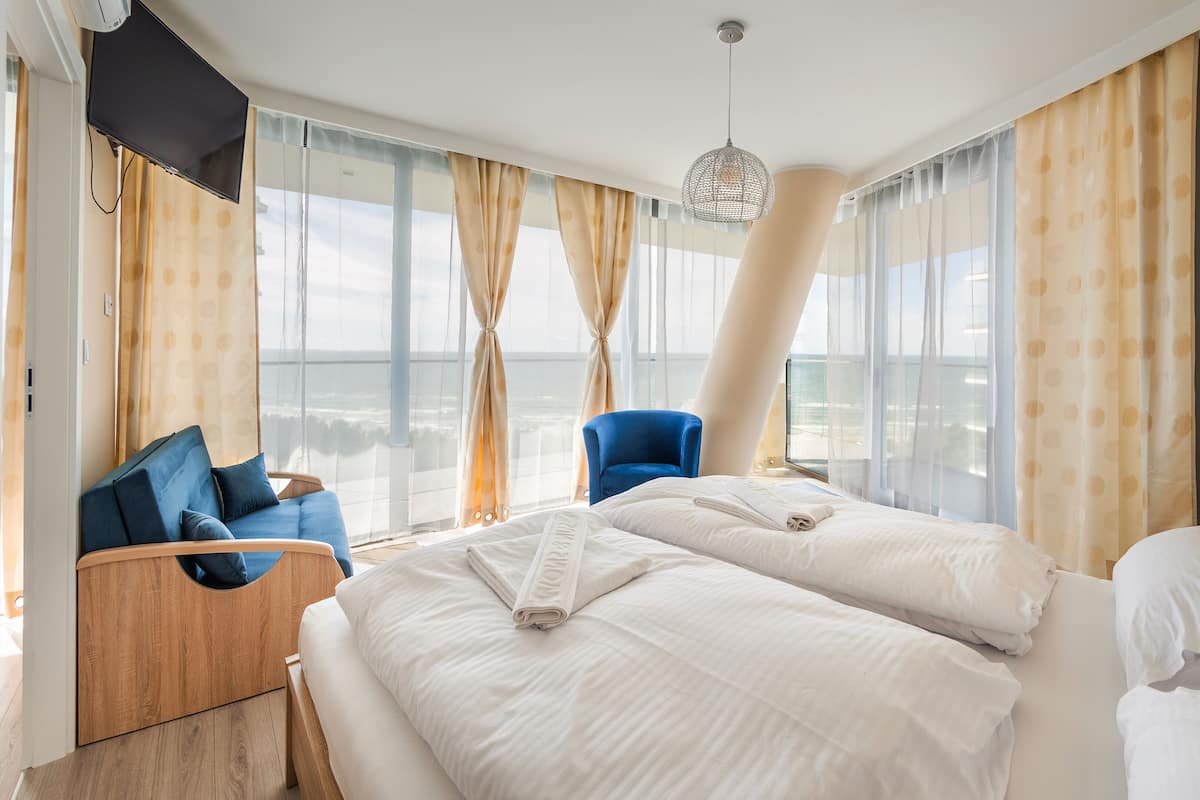 Een hotelkamer met een bed, een blauwe stoel, een houten nachtkastje en uitzicht op zee.