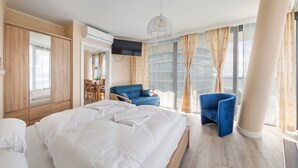 A hotel room with a large bed, a blue armchair, a TV, and a view of the city. - Prywatne Apartamenty Sun & Snow w Wave (Miedzyzdroje)